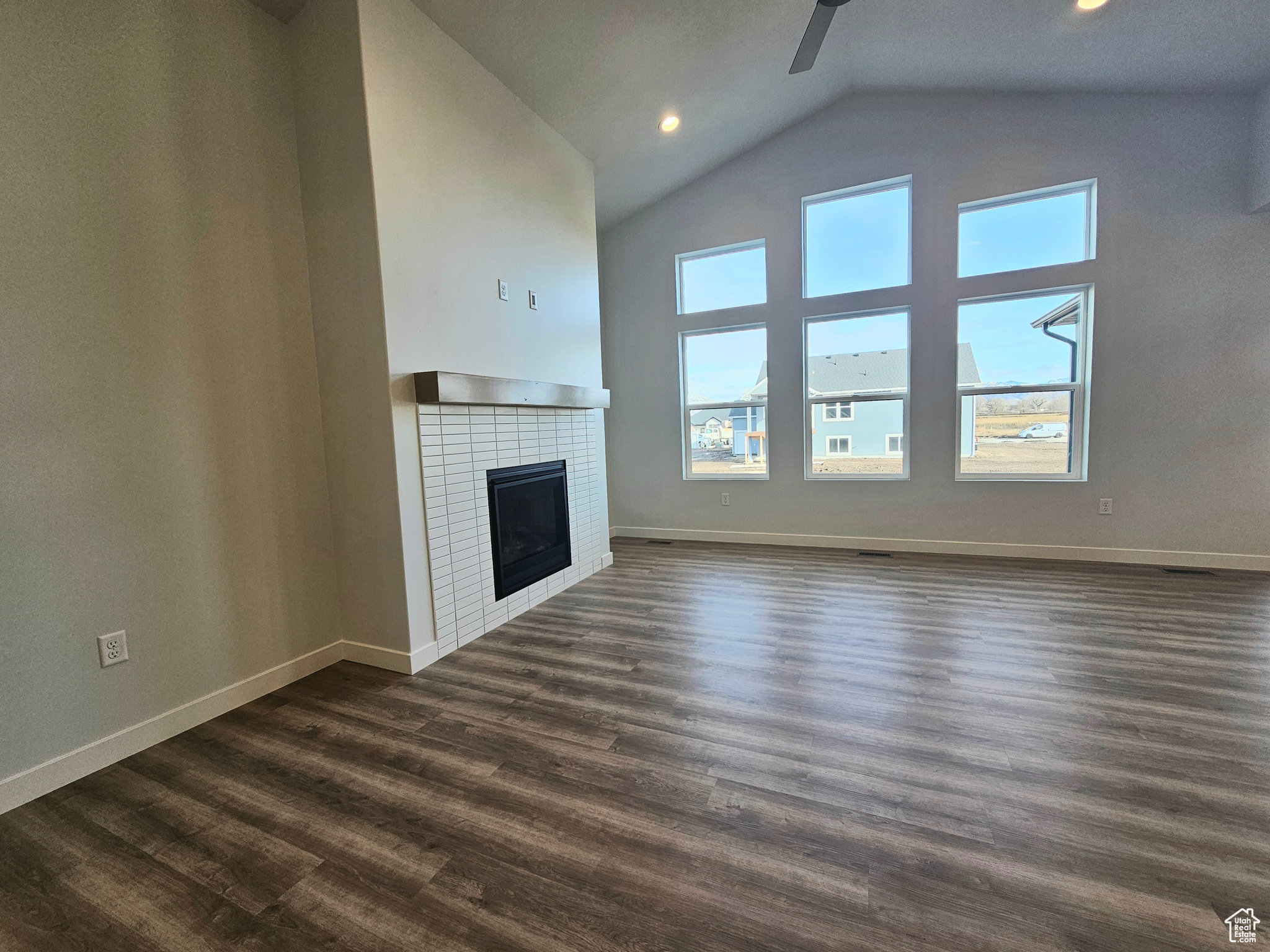 Unfurnished living room with ceiling fan, dark wood-type flooring, high vaulted ceiling, and a tiled fireplace