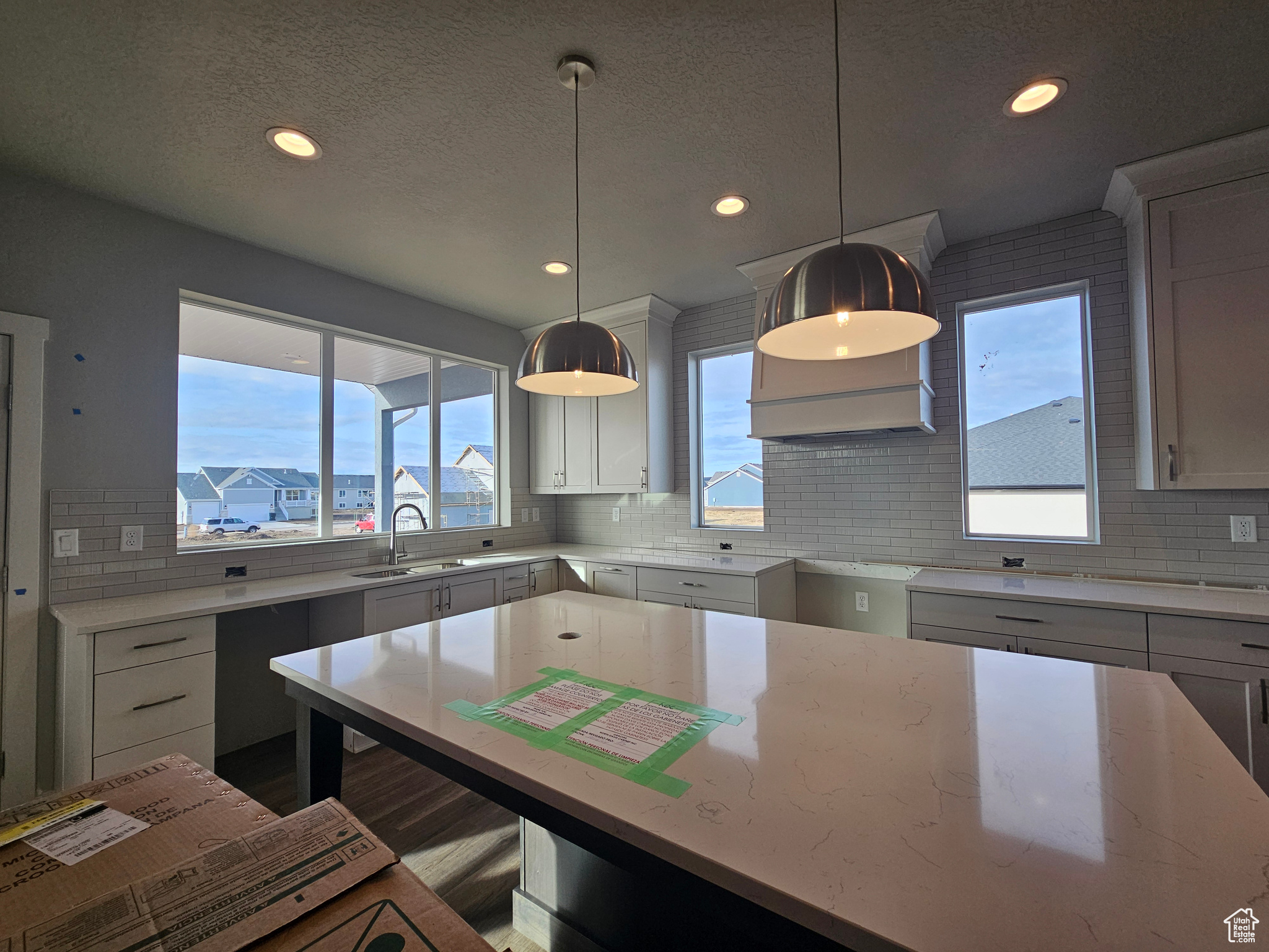 Kitchen with light stone countertops, decorative backsplash, sink, and pendant lighting