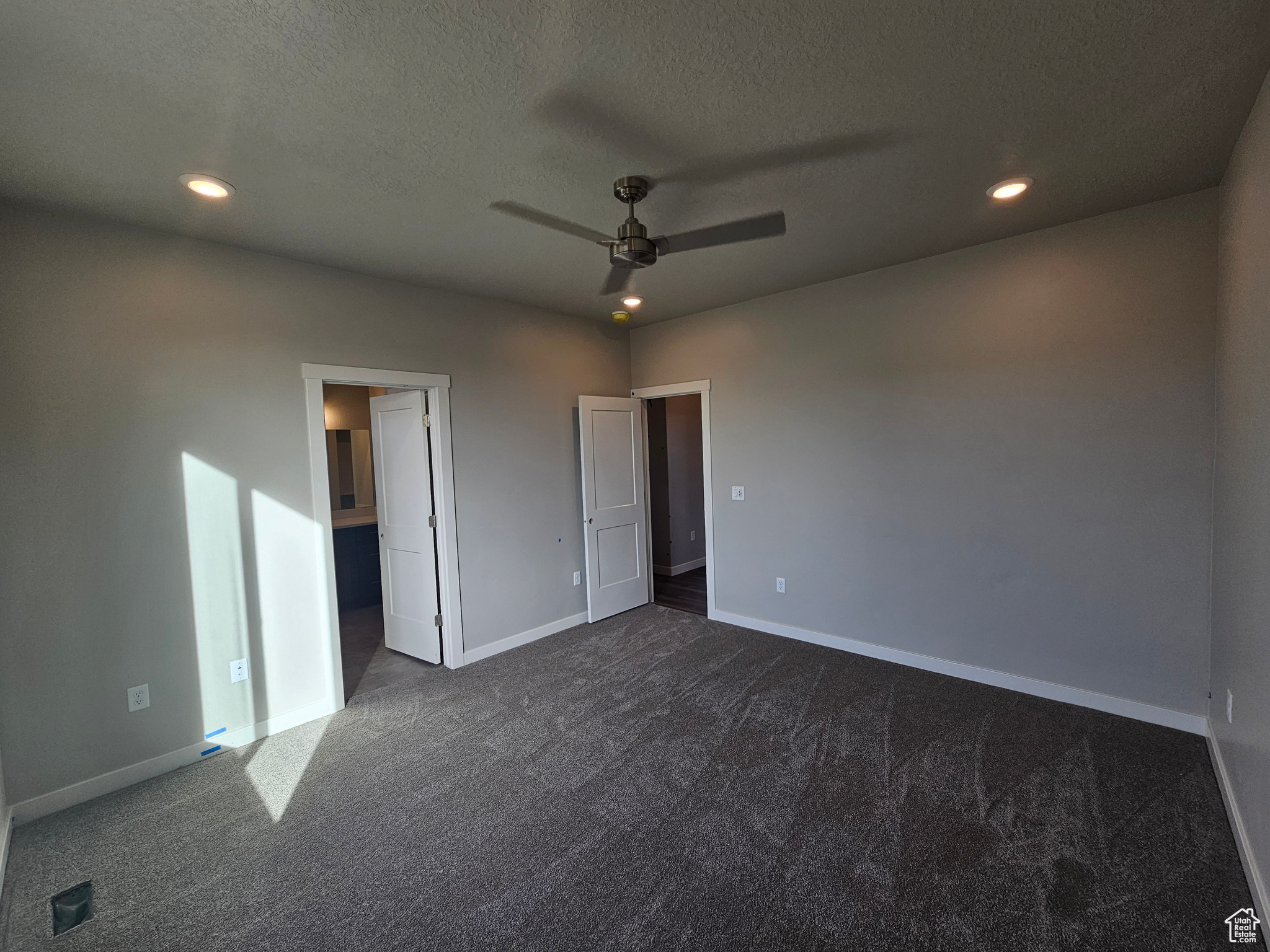 Unfurnished bedroom featuring dark colored carpet, ceiling fan, and a textured ceiling