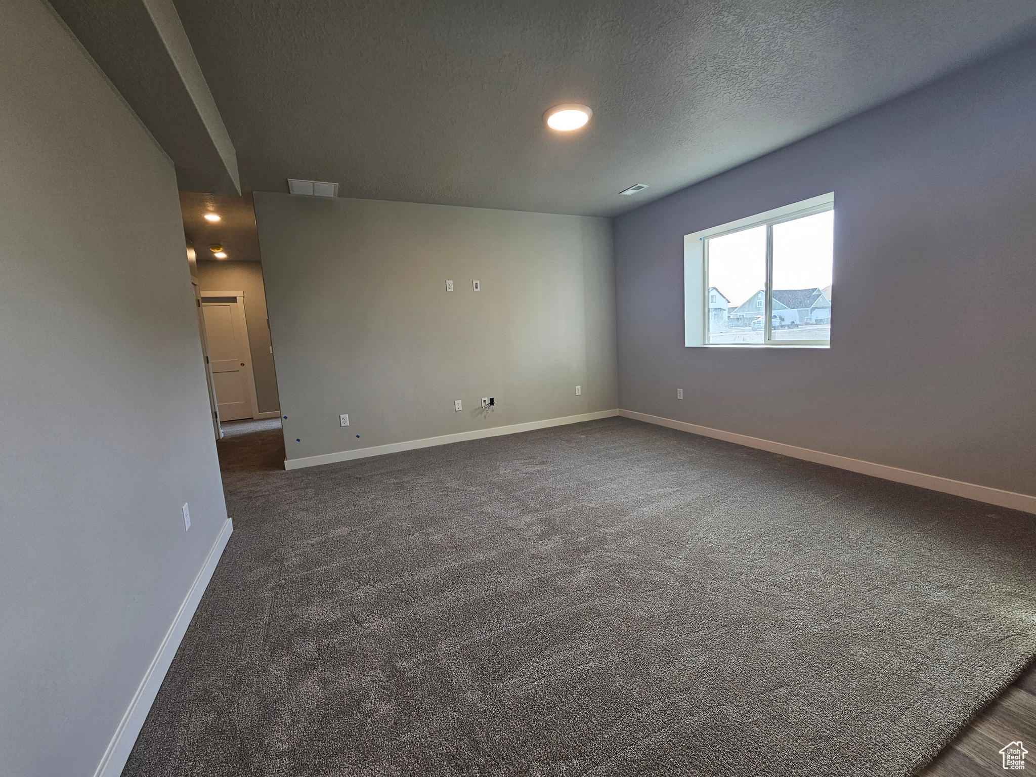 Unfurnished room featuring a textured ceiling and dark carpet