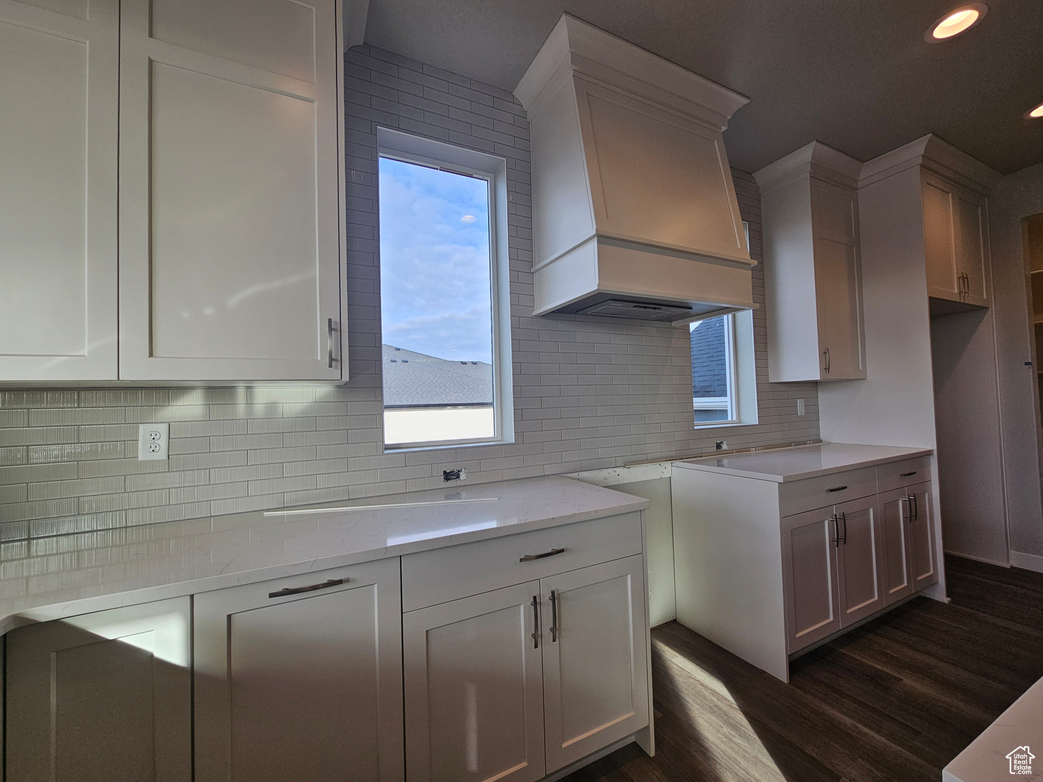 Kitchen with white cabinetry, dark hardwood / wood-style flooring, light stone countertops, and custom range hood