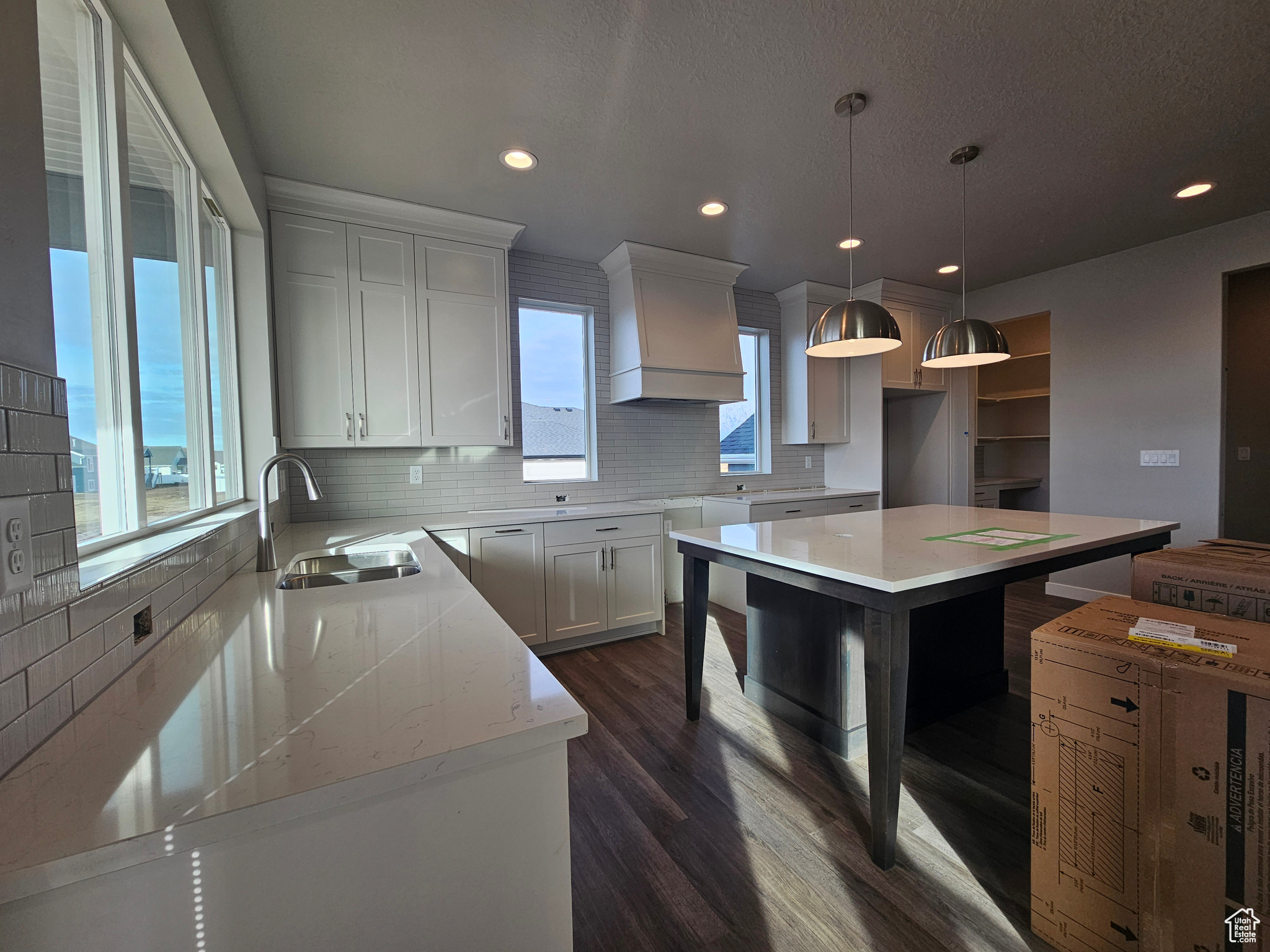 Kitchen featuring white cabinetry, sink, a center island, decorative light fixtures, and custom range hood