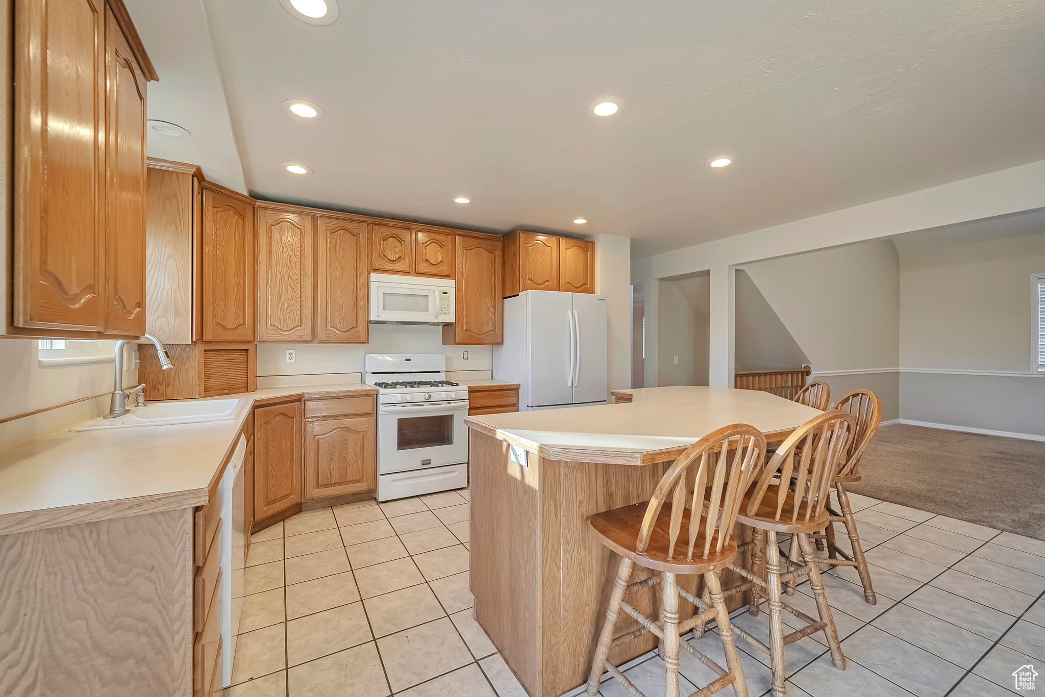 Kitchen with a kitchen breakfast bar, white appliances, sink, a center island, and light tile patterned flooring