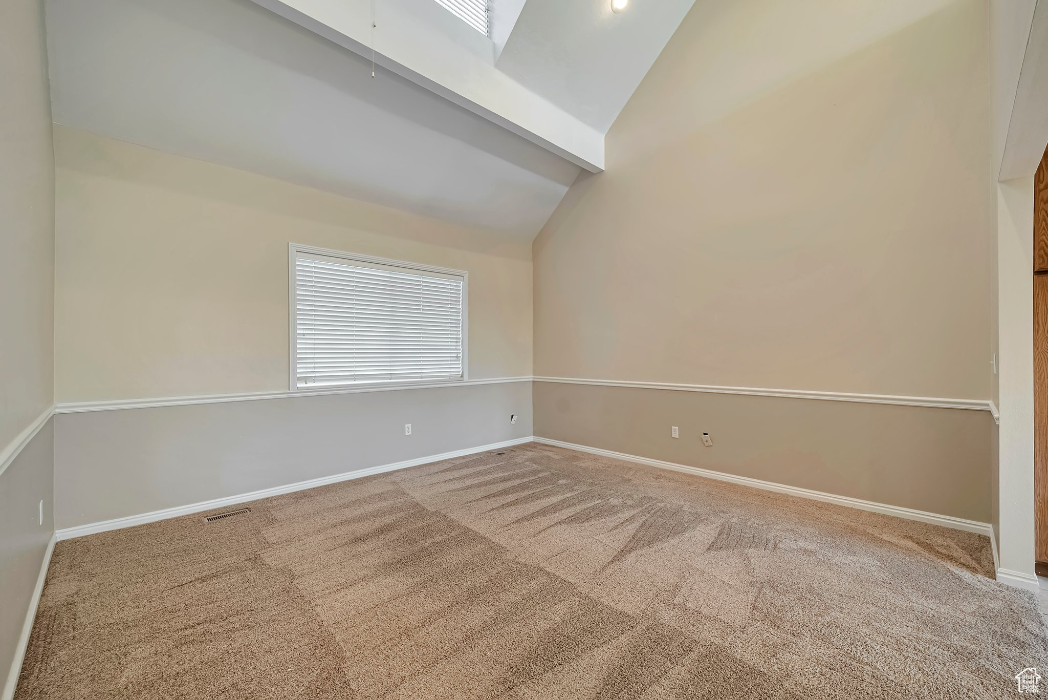 Carpeted empty room with beamed ceiling and high vaulted ceiling