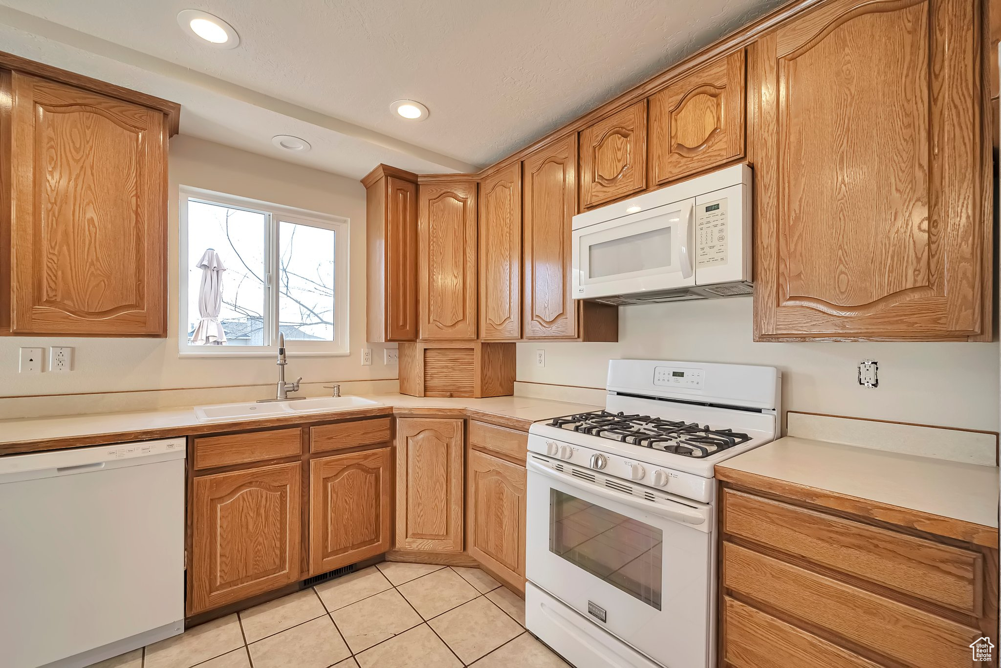 Kitchen with light tile patterned floors, white appliances, and sink