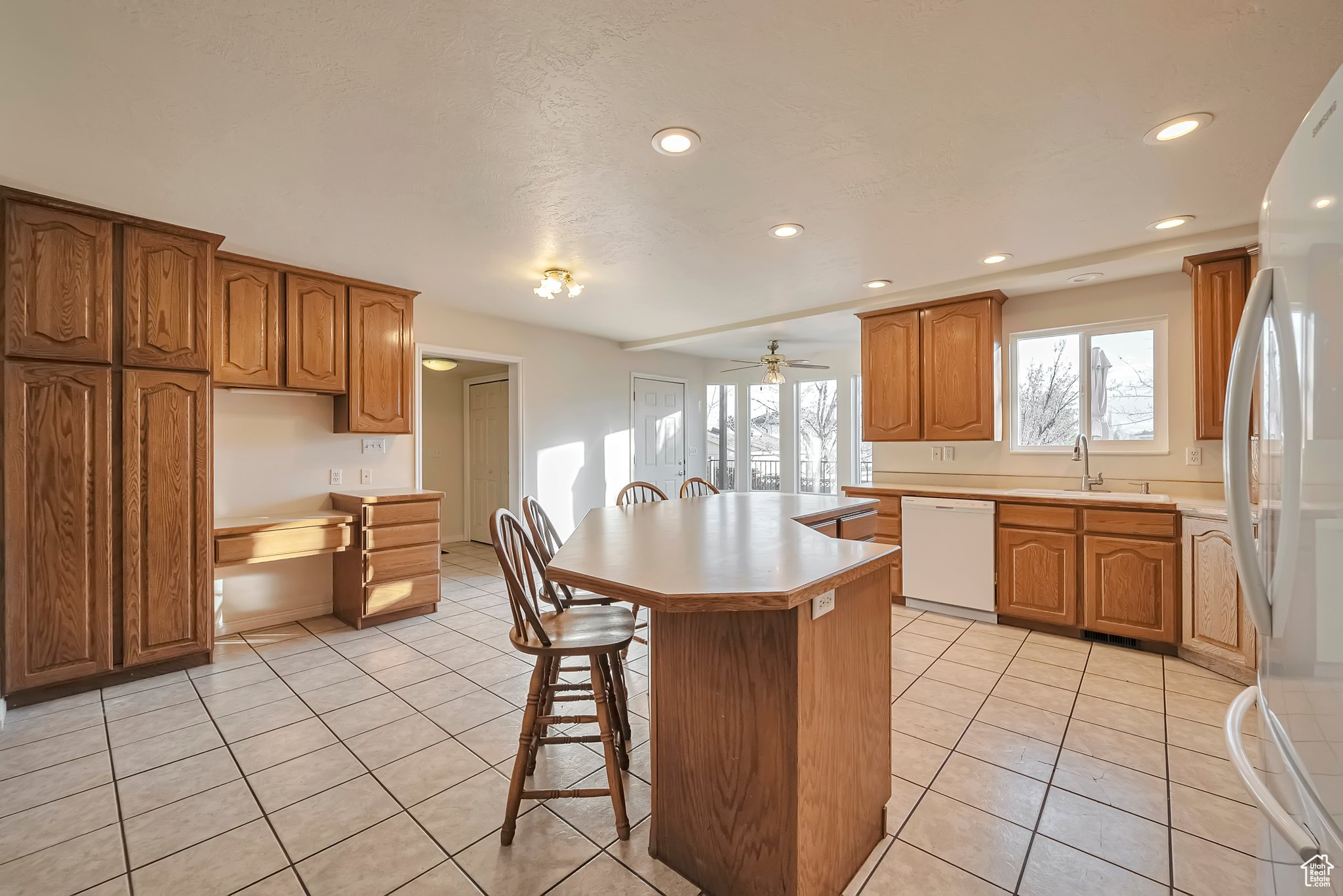 Kitchen with a kitchen bar, white appliances, sink, light tile patterned floors, and a kitchen island