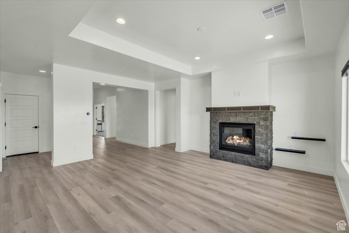 Unfurnished living room with a stone fireplace, a tray ceiling, and light hardwood / wood-style flooring