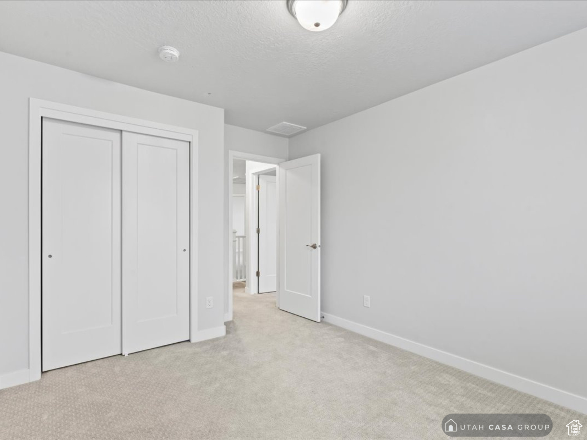 Unfurnished bedroom featuring light colored carpet, a textured ceiling, and a closet