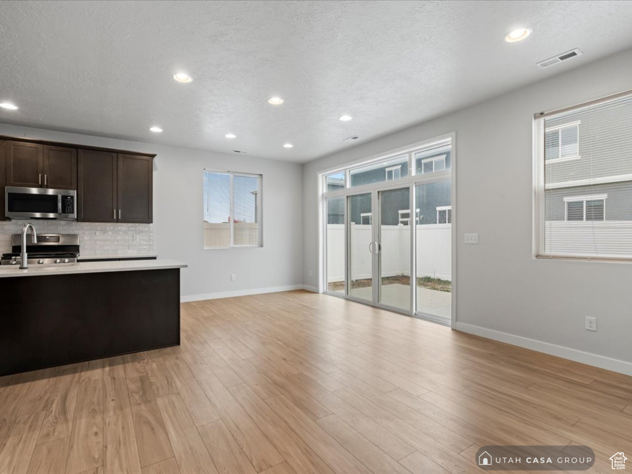 Kitchen featuring light hardwood / wood-style flooring, a textured ceiling, tasteful backsplash, dark brown cabinetry, and stainless steel appliances