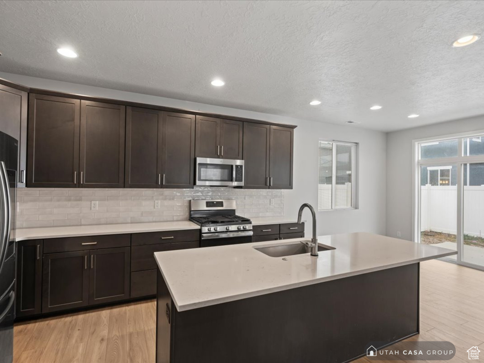 Kitchen featuring a textured ceiling, stainless steel appliances, a kitchen island with sink, sink, and light hardwood / wood-style flooring