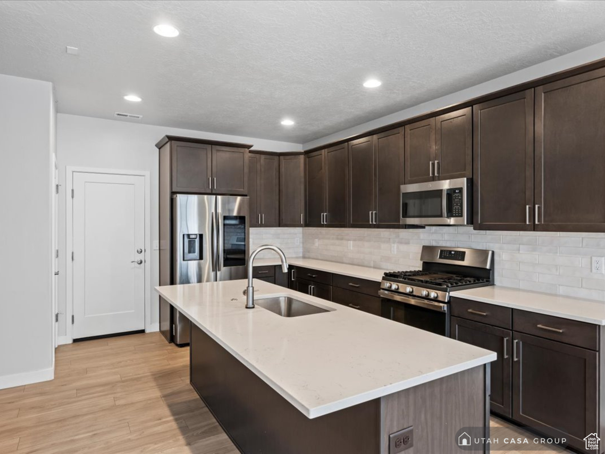 Kitchen with backsplash, a center island with sink, sink, appliances with stainless steel finishes, and dark brown cabinetry