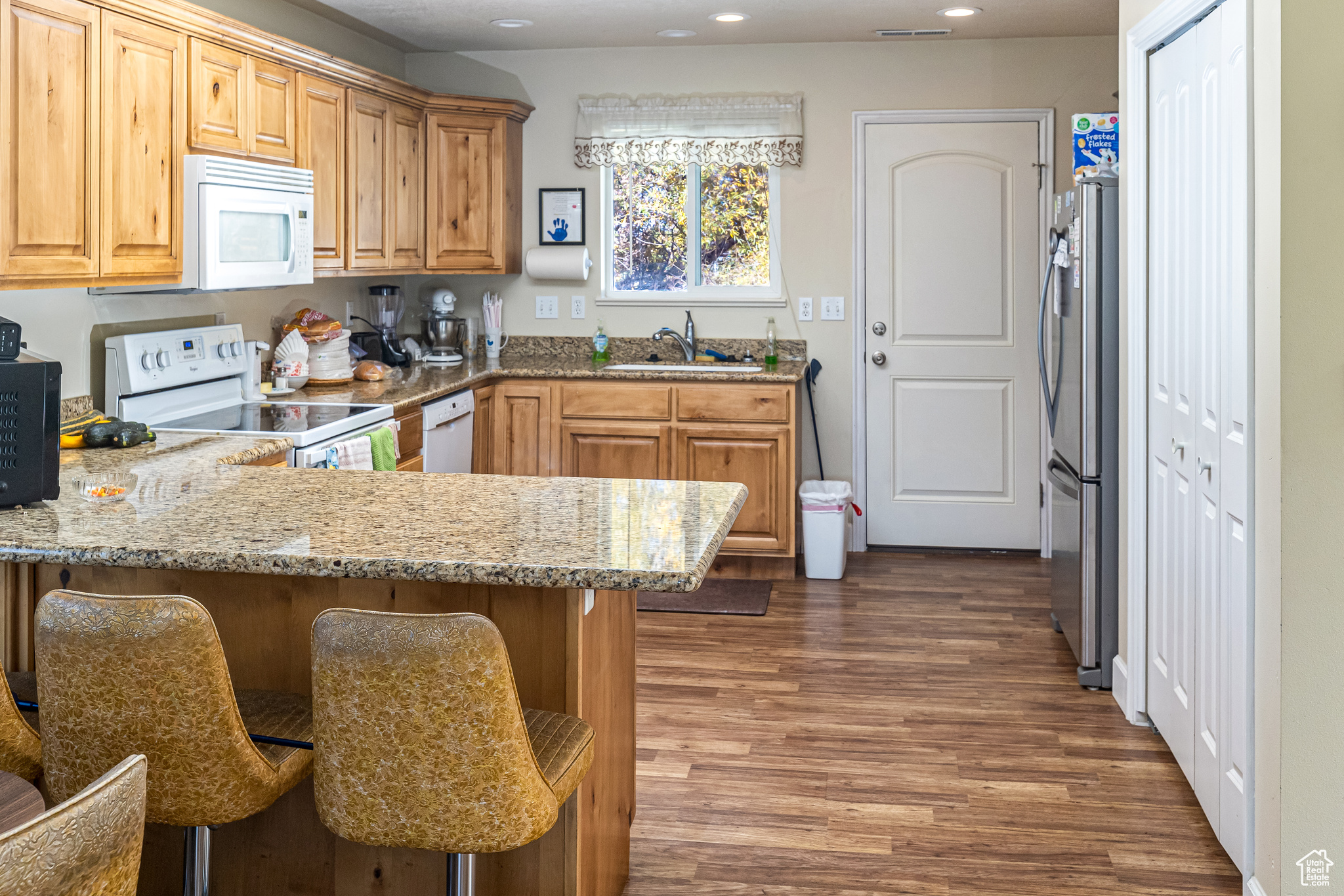 Kitchen with sink, dark hardwood / wood-style flooring, kitchen peninsula, white appliances, and a kitchen bar