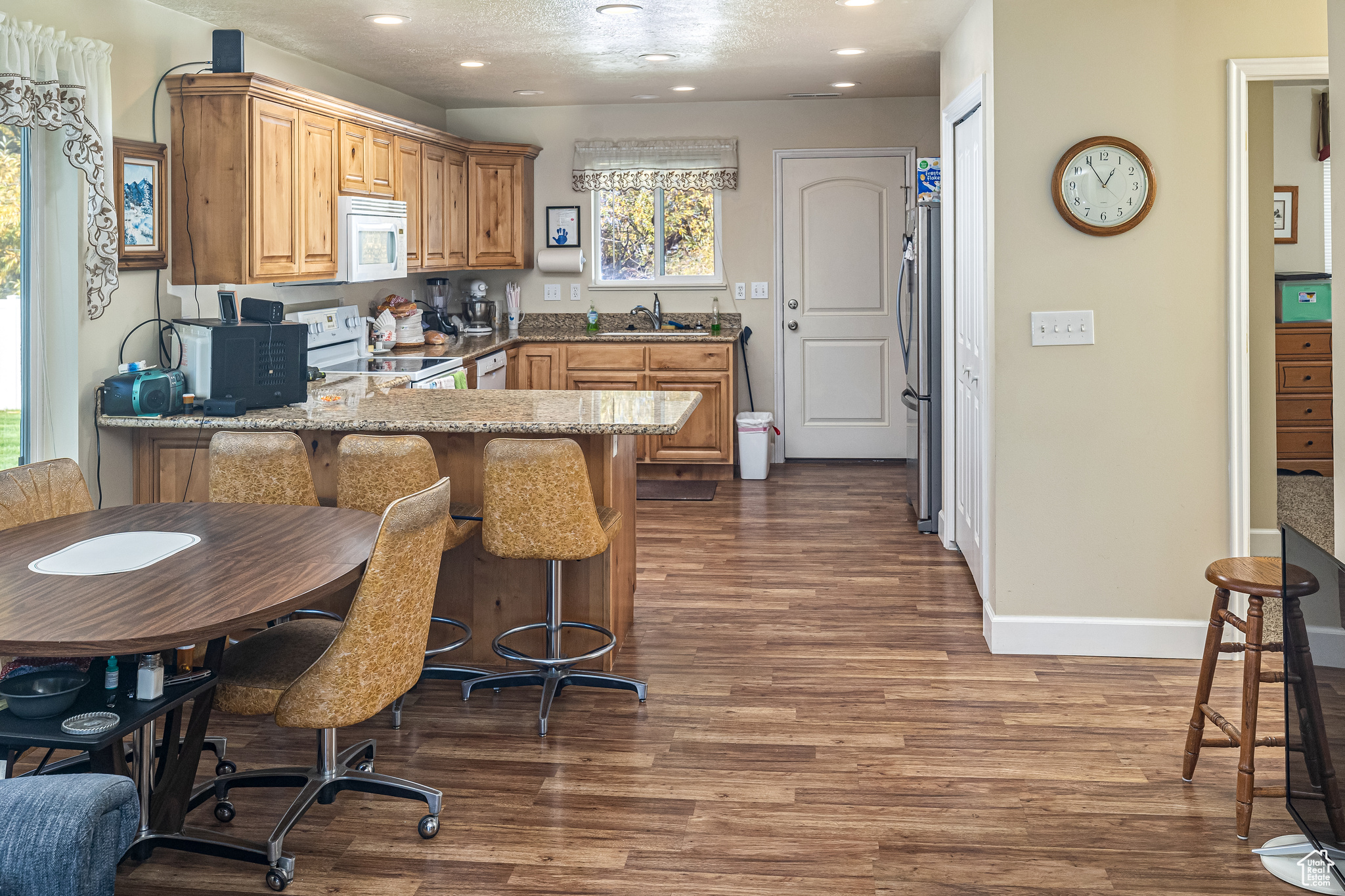 Kitchen with white appliances, dark wood-type flooring, sink, light stone countertops, and kitchen peninsula