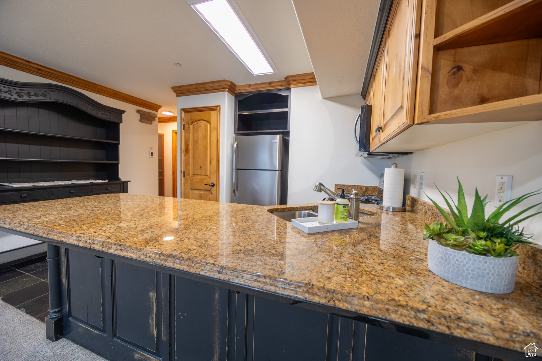 Kitchen with sink, crown molding, blue cabinetry, light stone counters, and stainless steel refrigerator