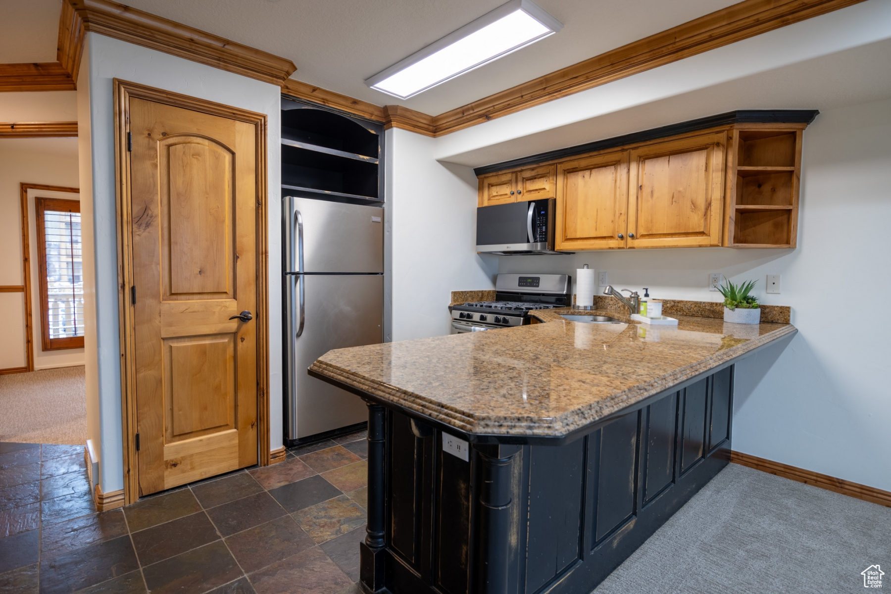 Kitchen featuring appliances with stainless steel finishes, light stone counters, crown molding, sink, and dark colored carpet