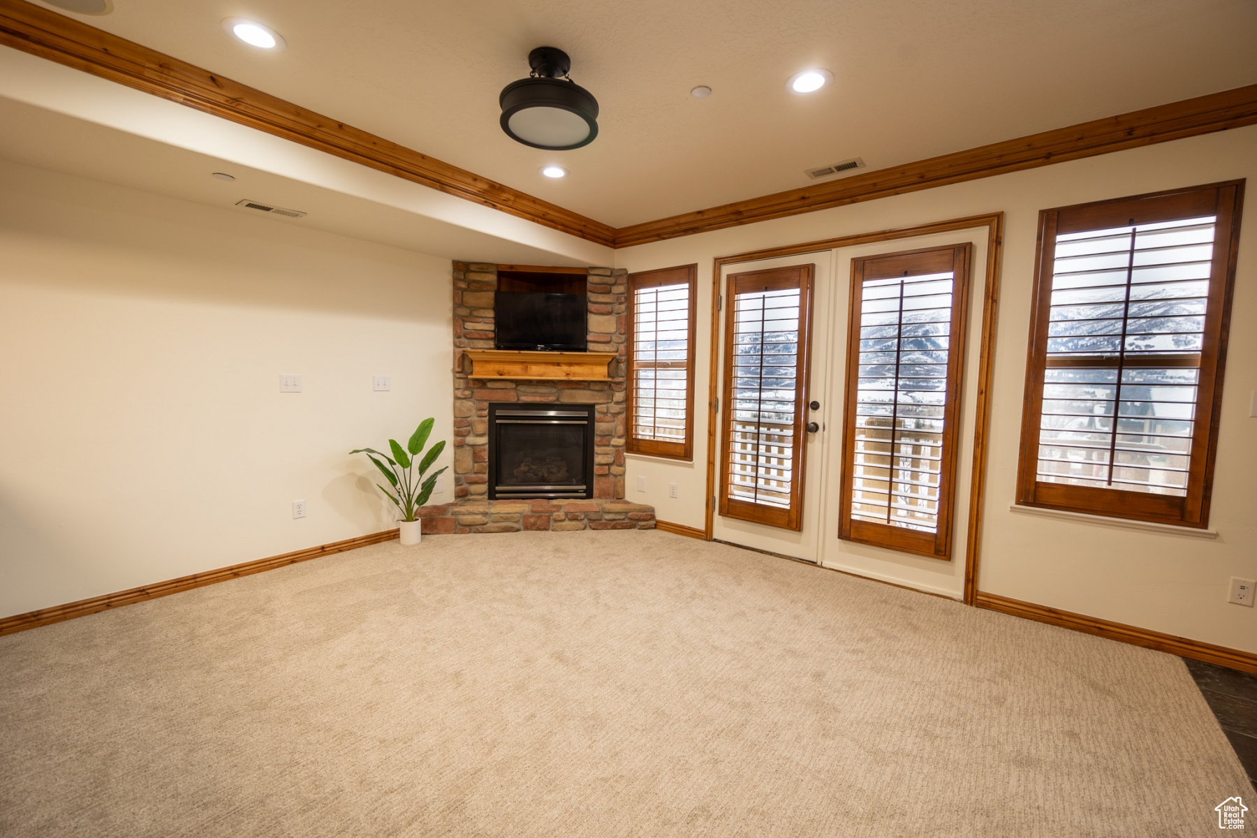 Unfurnished living room featuring a fireplace, french doors, carpet flooring, and ornamental molding