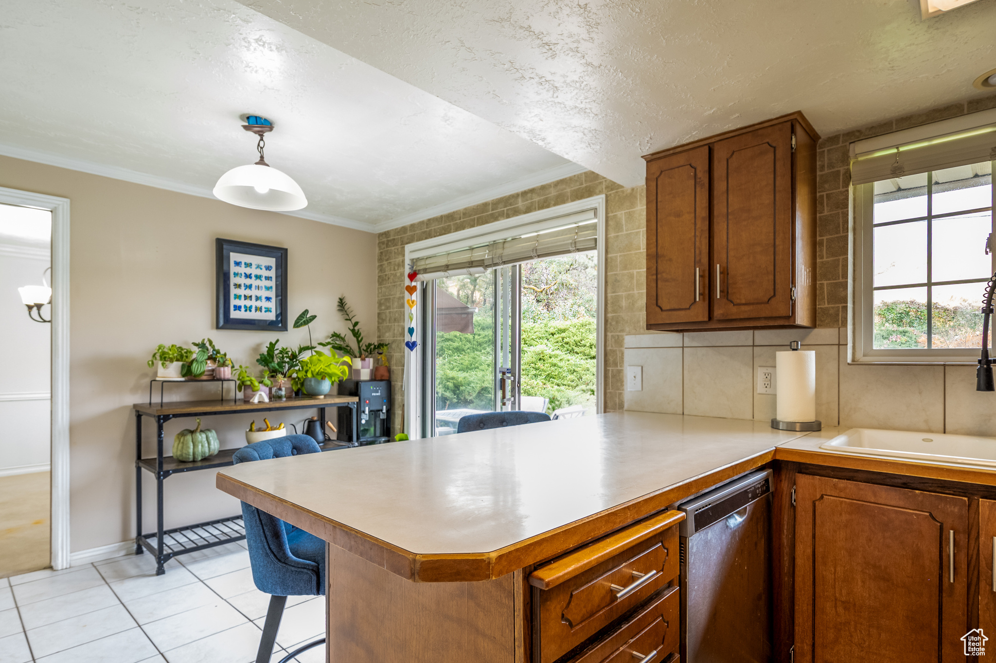 Kitchen featuring kitchen peninsula, ornamental molding, light tile patterned floors, dishwasher, and hanging light fixtures