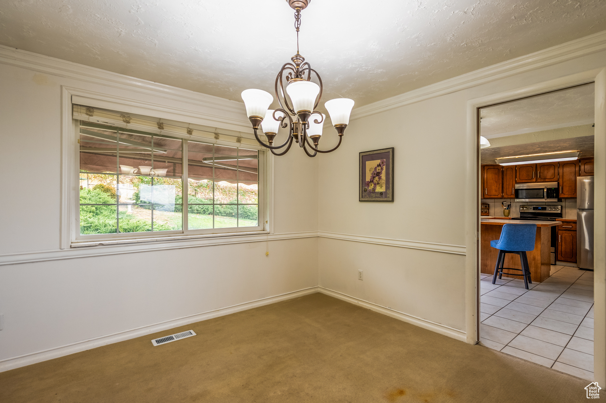 Empty room with light colored carpet, ornamental molding, and a chandelier