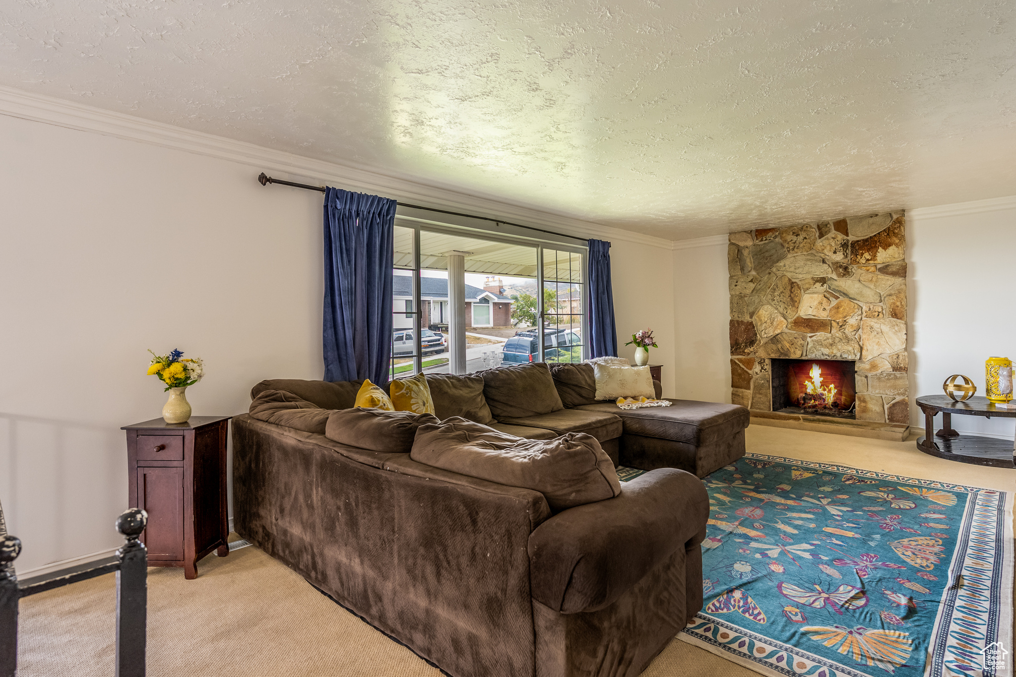 Living room with a stone fireplace, light carpet, crown molding, and a textured ceiling