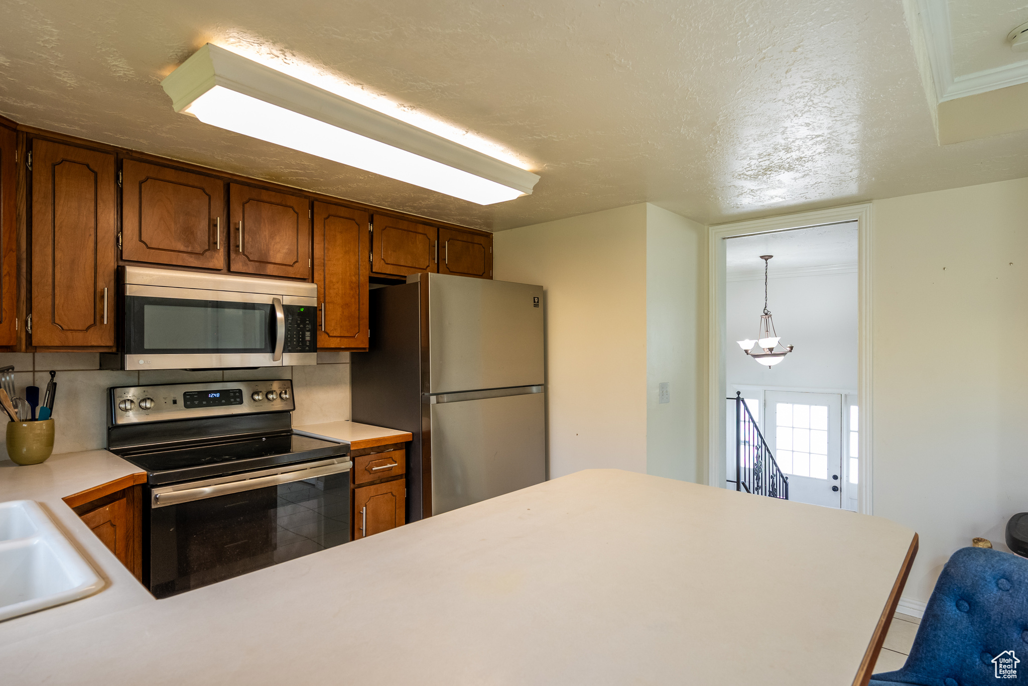 Kitchen with pendant lighting, backsplash, sink, a textured ceiling, and stainless steel appliances