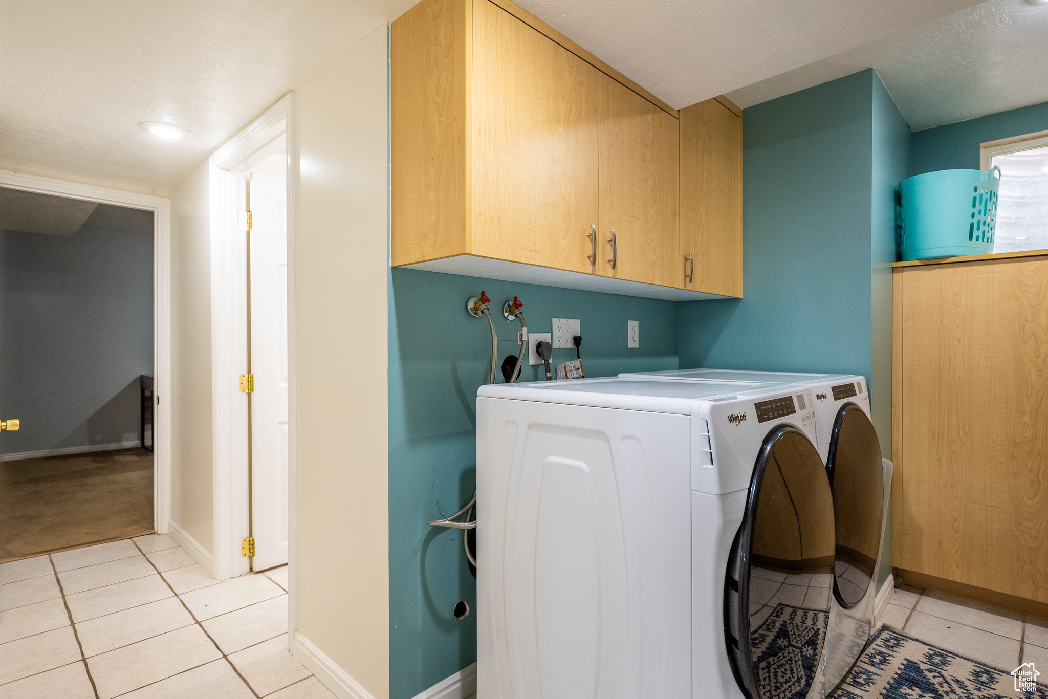 Laundry area with washing machine and dryer, light tile patterned floors, and cabinets