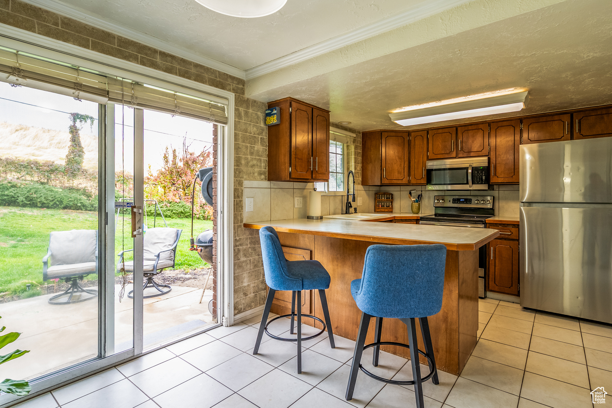 Kitchen with sink, light tile patterned floors, appliances with stainless steel finishes, kitchen peninsula, and a breakfast bar area