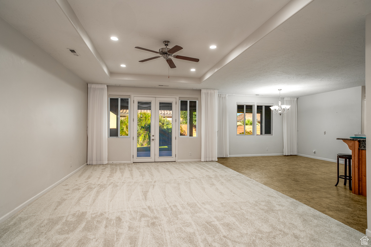 Unfurnished living room with ceiling fan with notable chandelier, light tile patterned flooring, a raised ceiling, and french doors