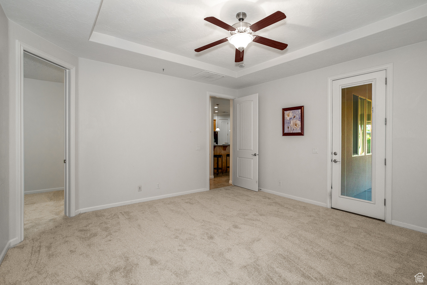 Unfurnished bedroom featuring a raised ceiling, access to exterior, ceiling fan, and light carpet