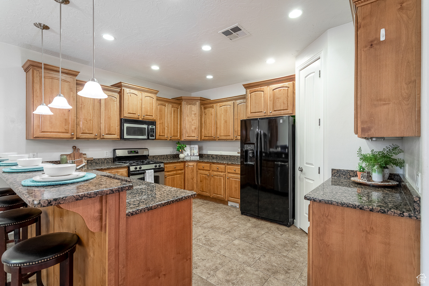 Kitchen featuring stainless steel appliances, a kitchen breakfast bar, dark stone countertops, kitchen peninsula, and decorative light fixtures