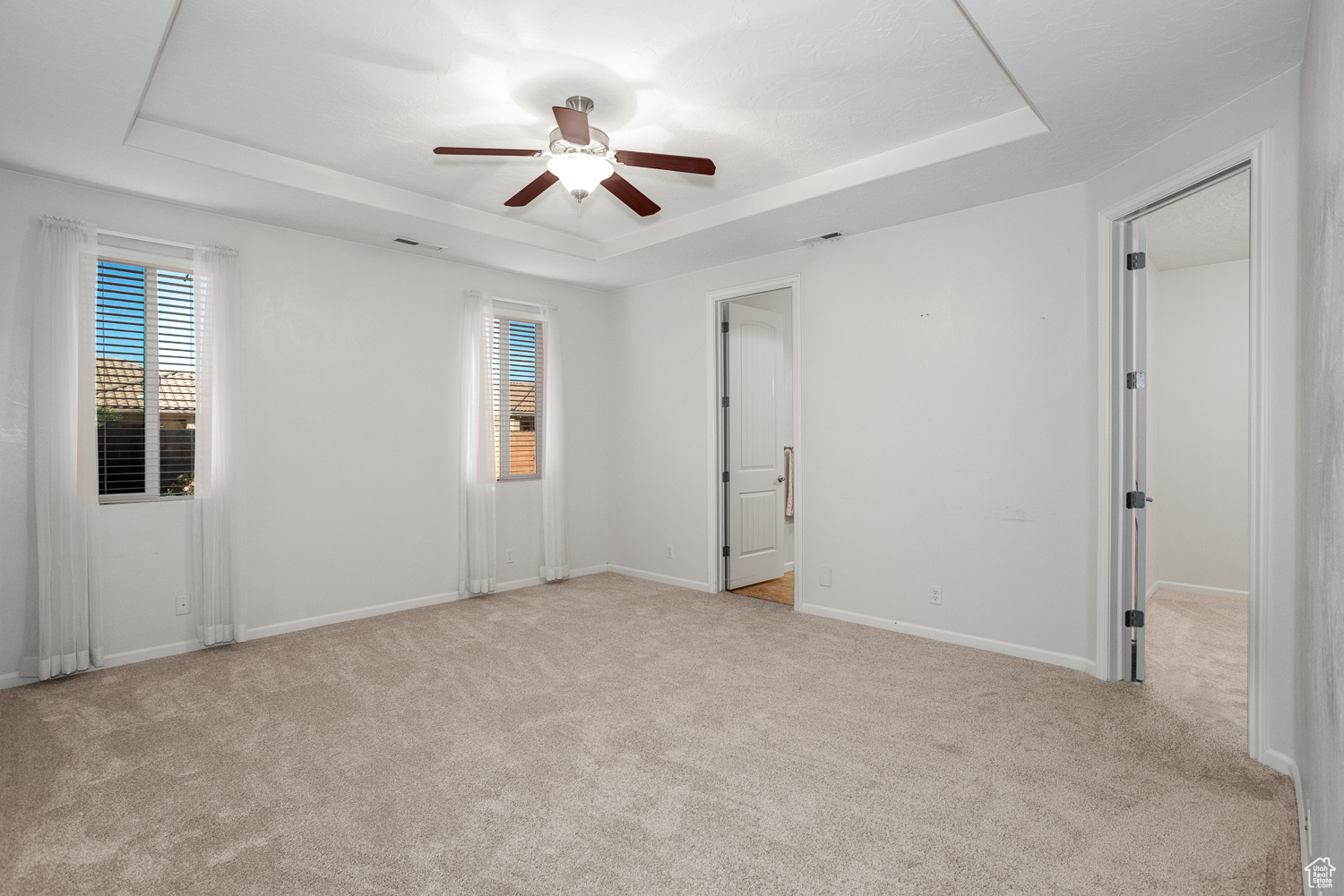 Unfurnished room with a raised ceiling, light carpet, and ceiling fan