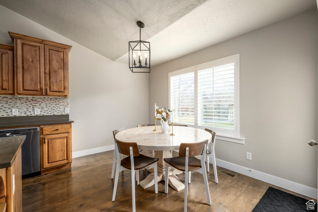 Dining space with a textured ceiling, dark hardwood / wood-style flooring, a chandelier, and vaulted ceiling