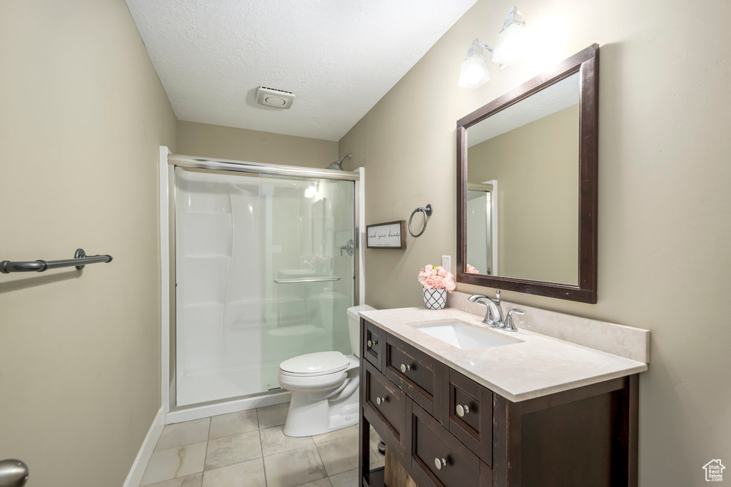 Bathroom with an enclosed shower, vanity, a textured ceiling, tile patterned flooring, and toilet