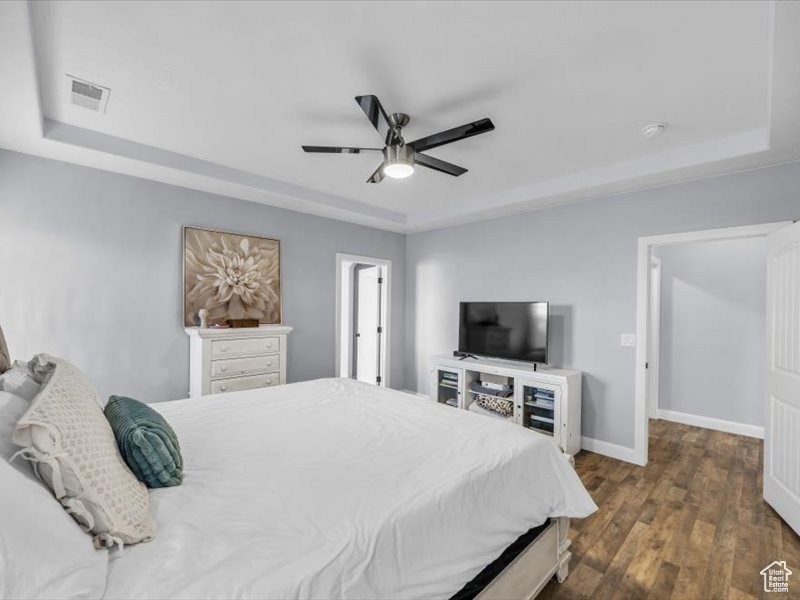 Bedroom with ceiling fan, dark hardwood / wood-style flooring, and a raised ceiling