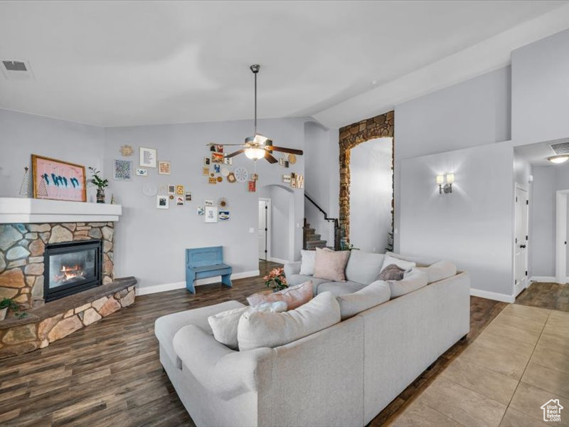 Living room with wood-type flooring, vaulted ceiling, a stone fireplace, and ceiling fan