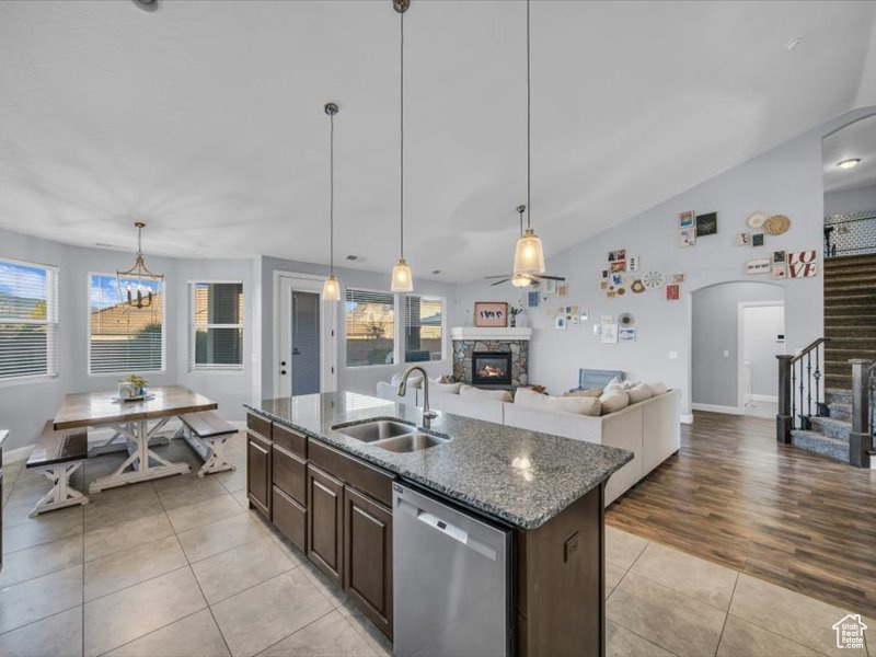 Kitchen featuring stainless steel dishwasher, dark brown cabinetry, sink, a stone fireplace, and an island with sink