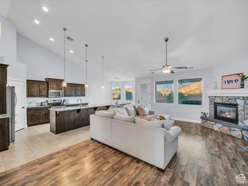 Living room featuring a high ceiling, light hardwood / wood-style floors, a stone fireplace, and ceiling fan