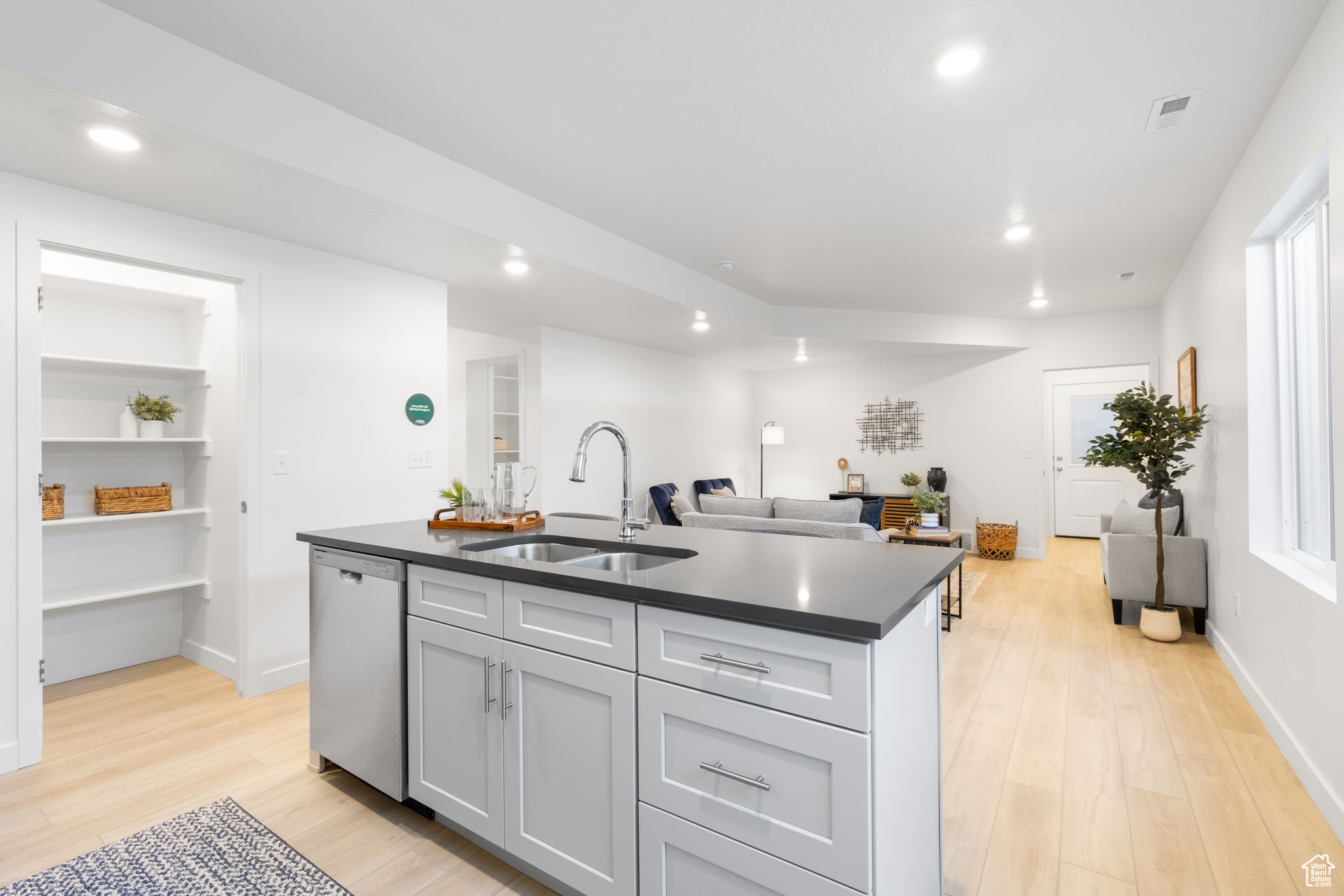 Kitchen with dishwasher, sink, built in features, light hardwood / wood-style floors, and a kitchen island with sink