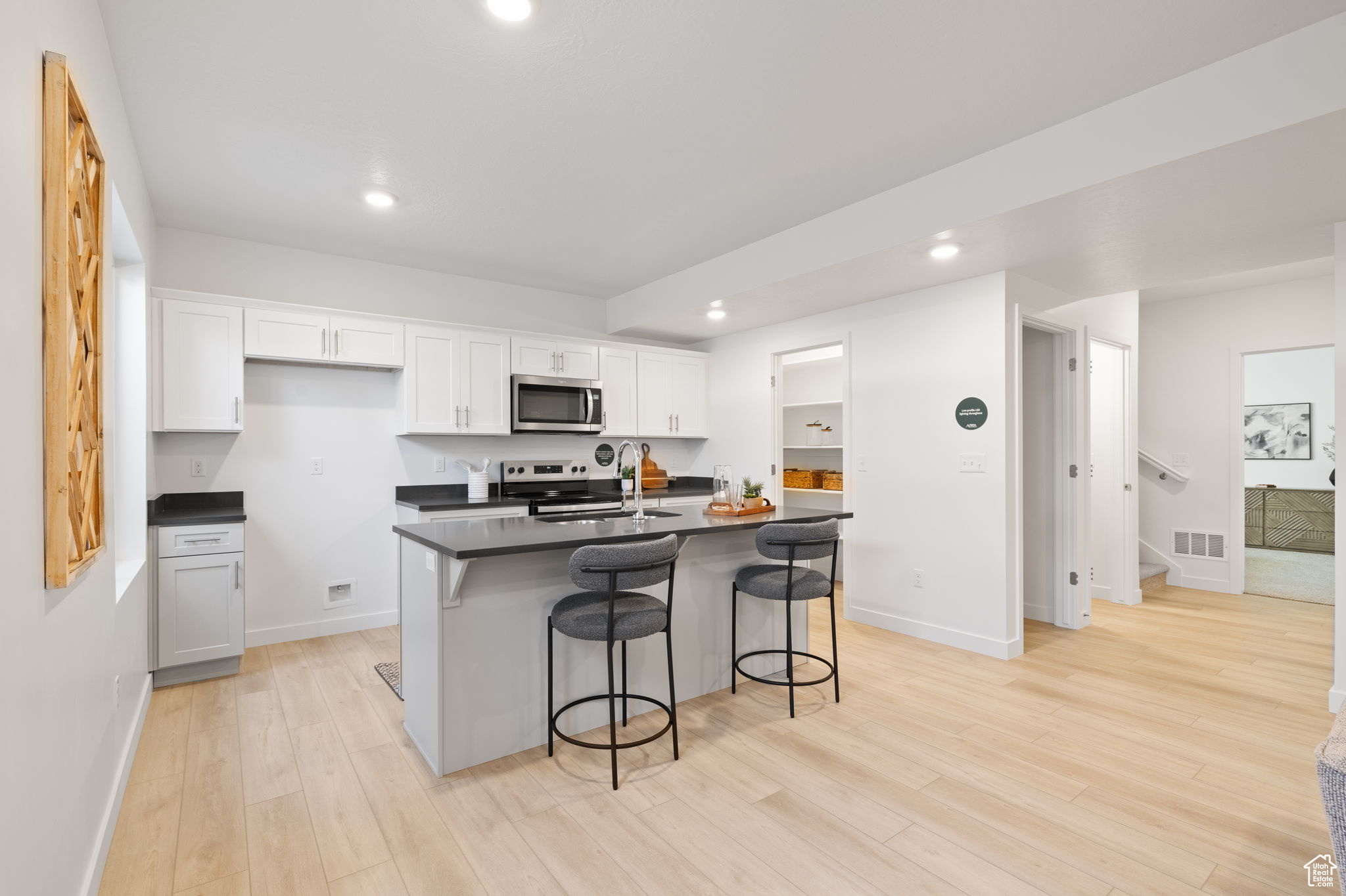 Kitchen featuring a breakfast bar area, white cabinets, an island with sink, and appliances with stainless steel finishes