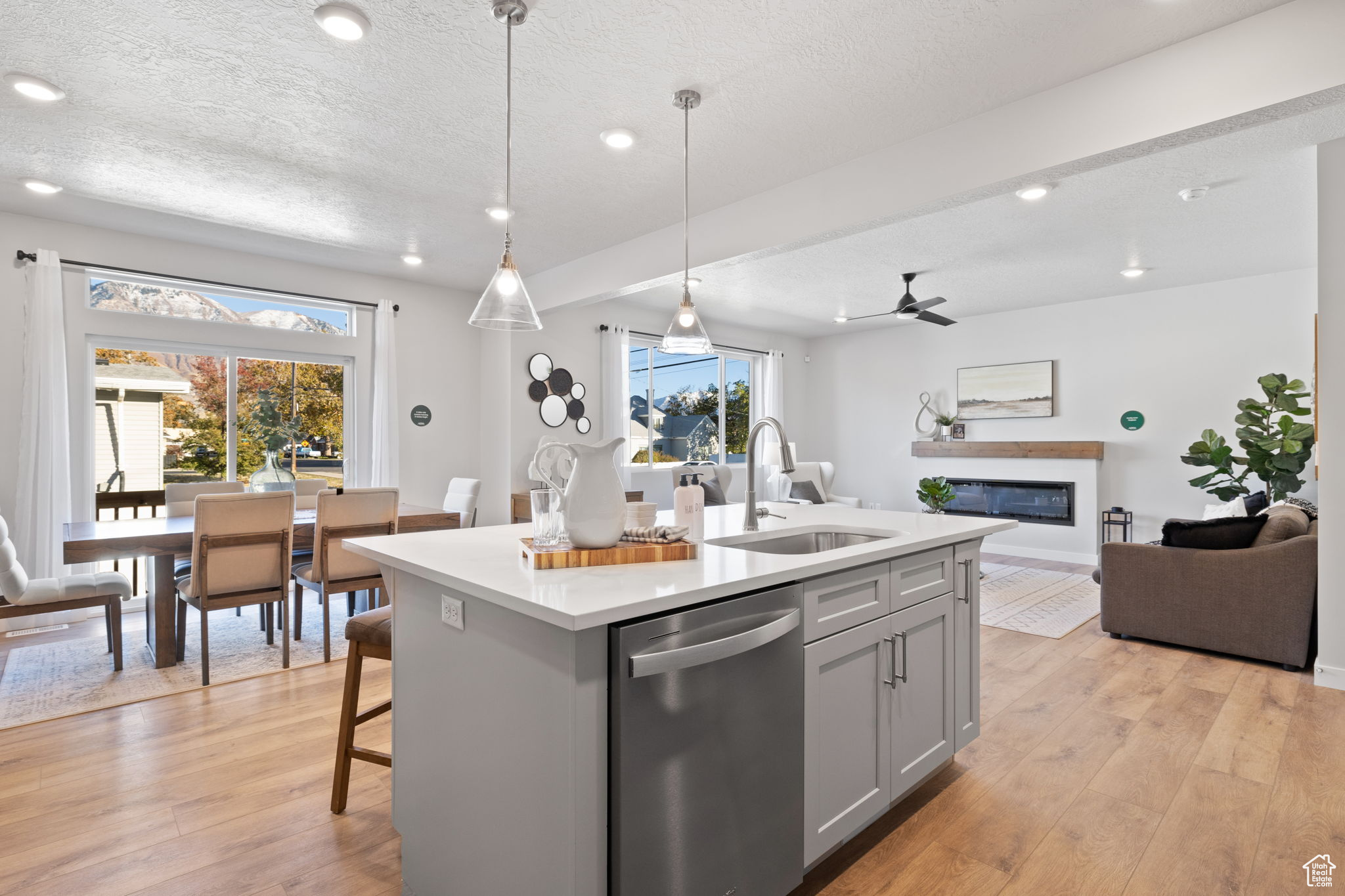 Kitchen featuring pendant lighting, dishwasher, sink, ceiling fan, and an island with sink