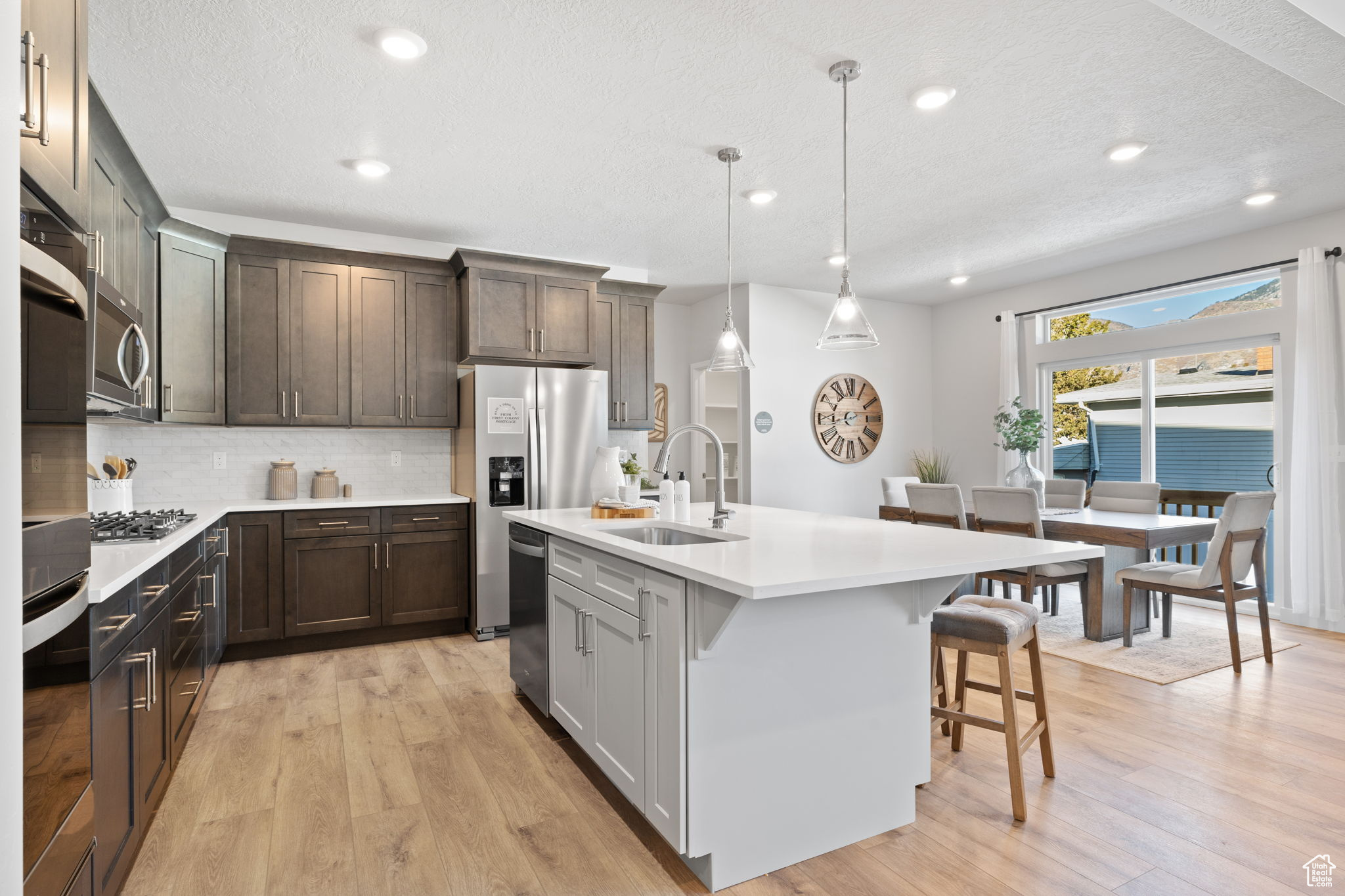 Kitchen featuring tasteful backsplash, sink, pendant lighting, a center island with sink, and light hardwood / wood-style flooring