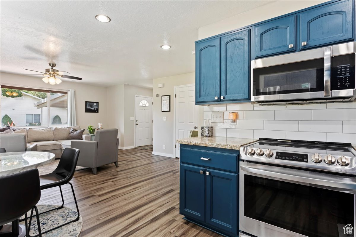 Kitchen with light stone countertops, backsplash, stainless steel appliances, and blue cabinets