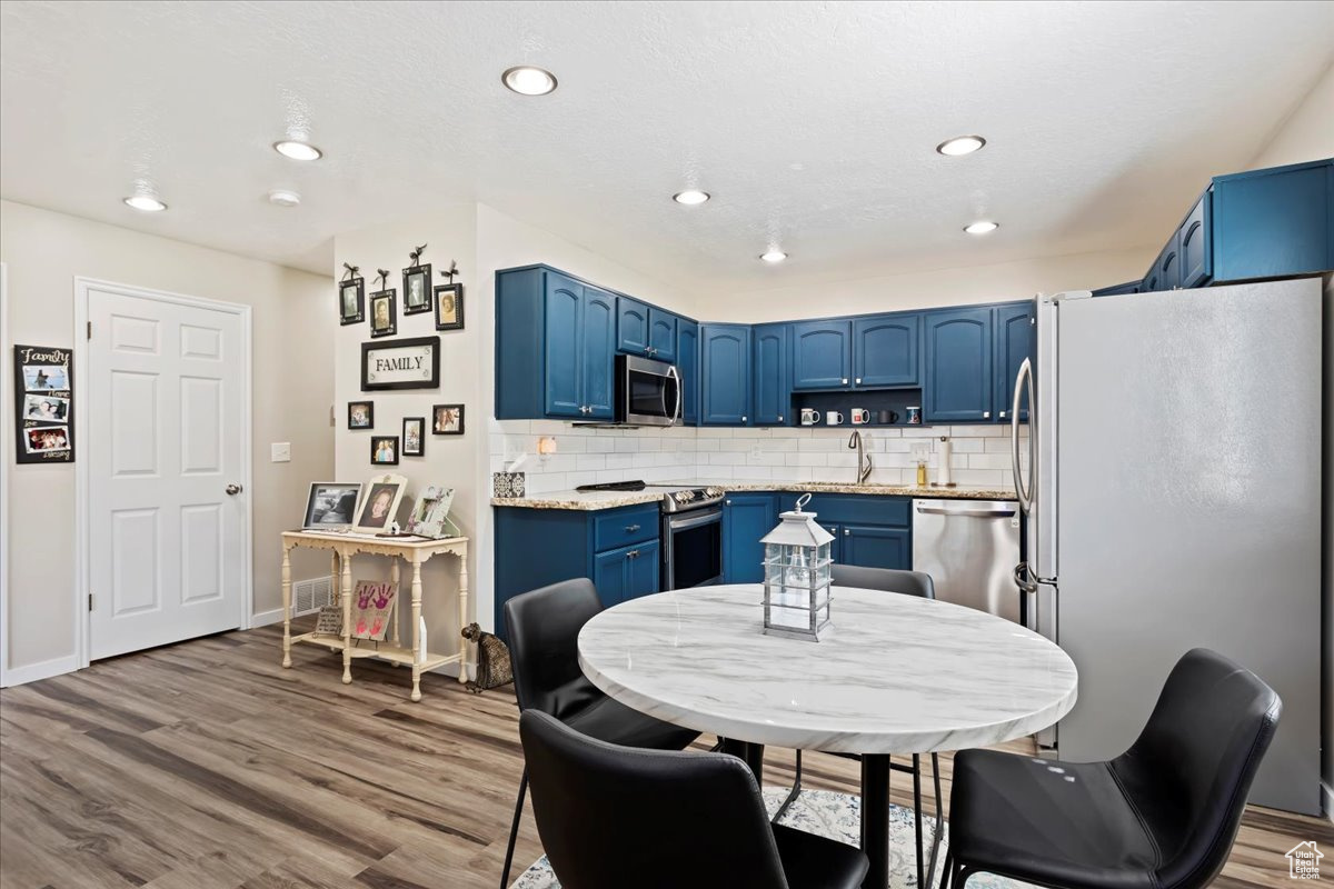 Kitchen featuring backsplash, sink, hardwood / wood-style flooring, blue cabinetry, and appliances with stainless steel finishes