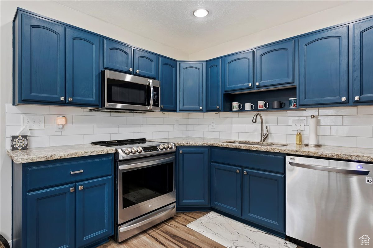 Kitchen featuring appliances with stainless steel finishes, light stone counters, blue cabinets, sink, and light hardwood / wood-style floors