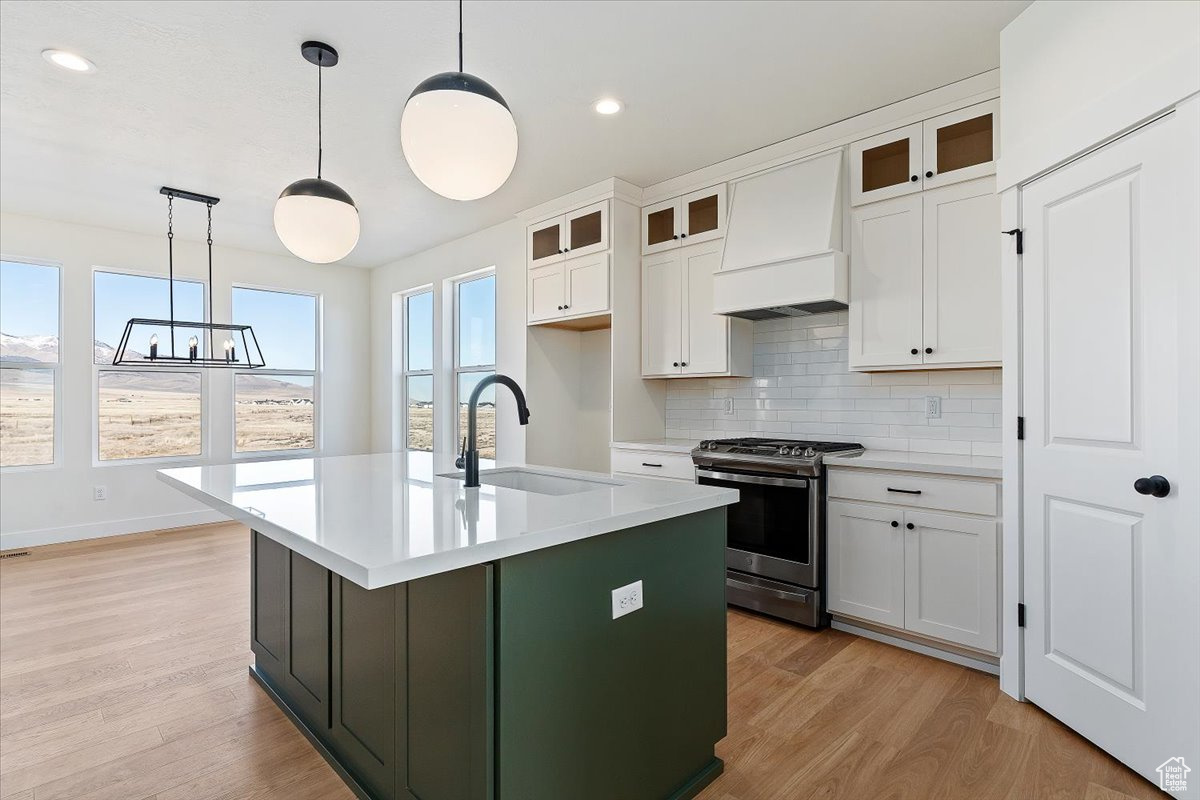 Kitchen with stainless steel gas range, exhaust hood, white cabinets, and designer light fixtures