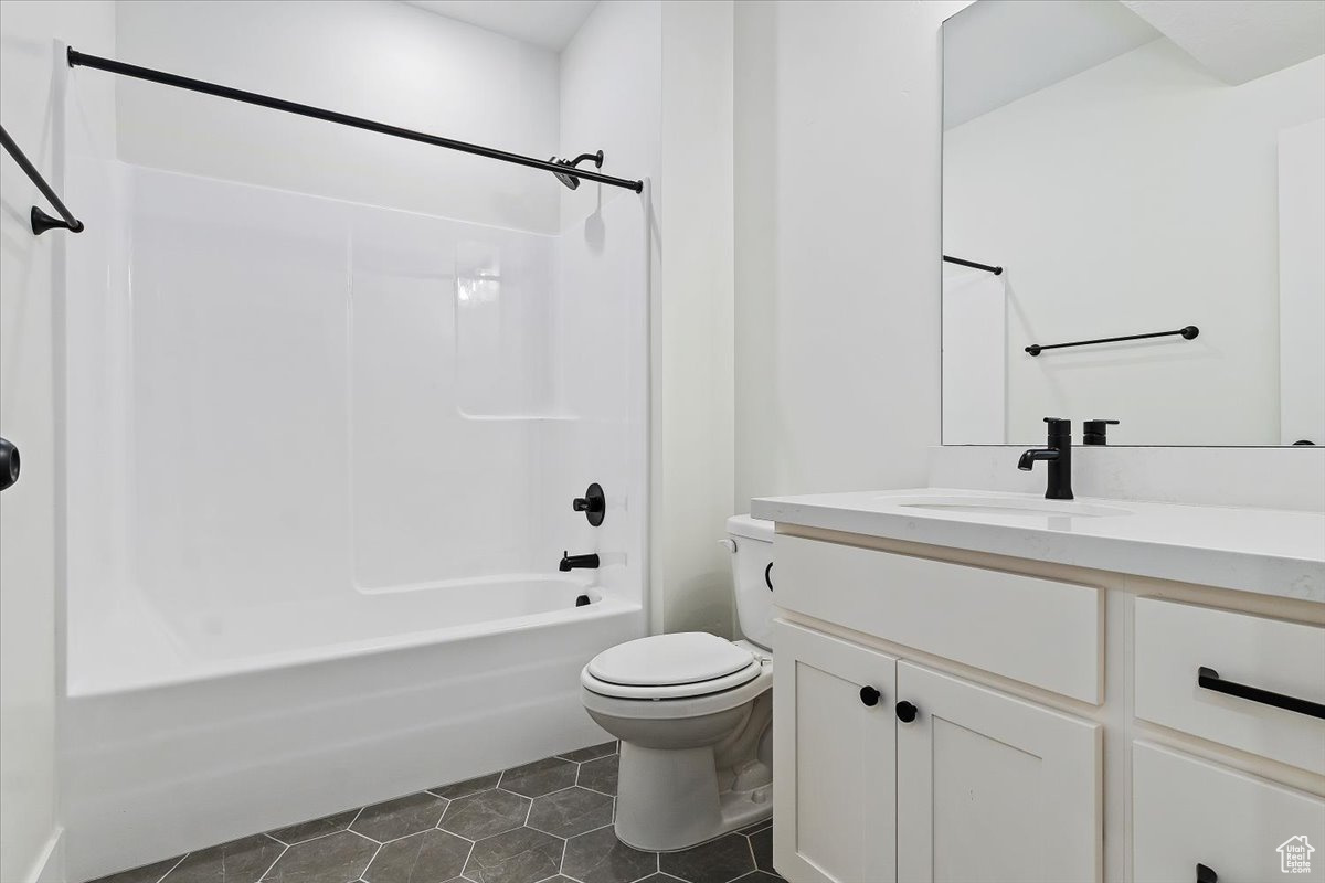 Basement bathroom with tile patterned floors, vanity, bathtub / shower combination, and toilet