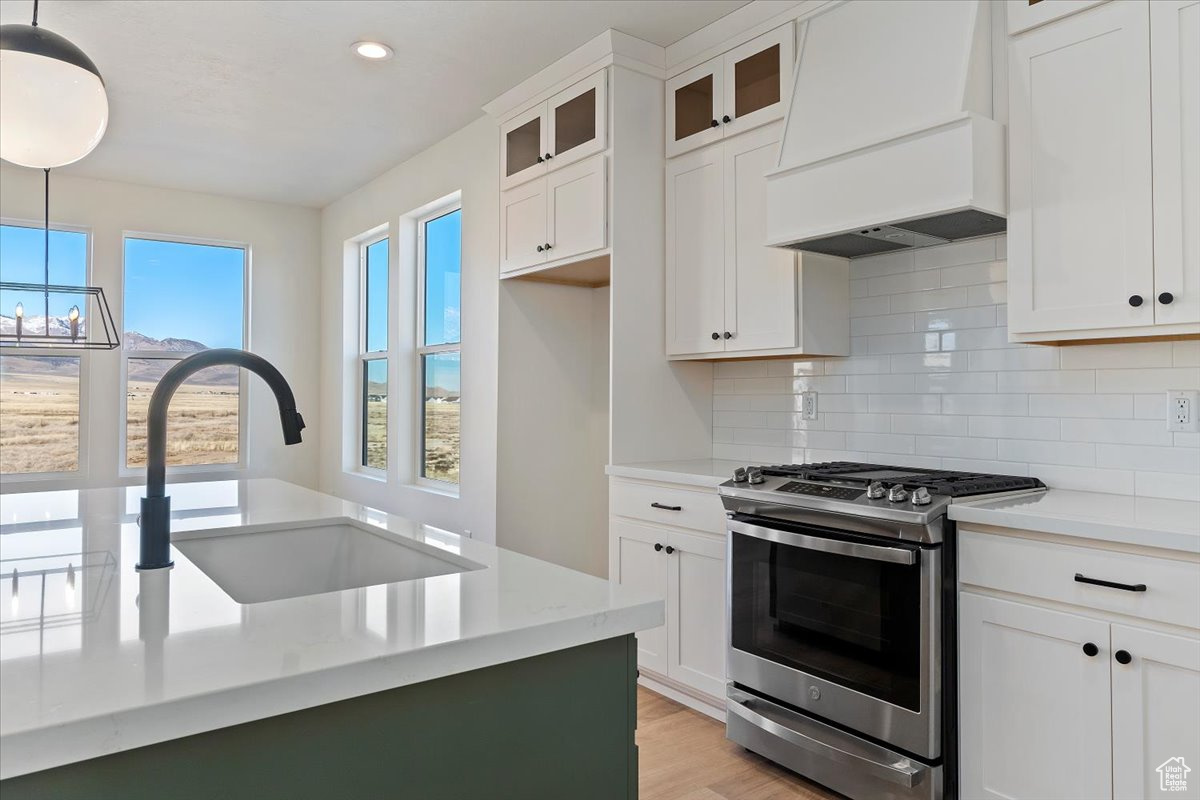 Kitchen with stainless steel gas range, exhaust hood, white cabinets, and designer light fixtures