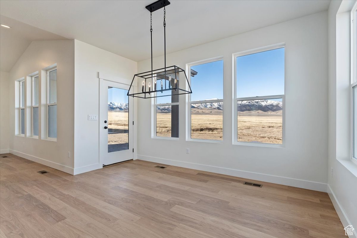 Unfurnished dining area with a mountain view, light hardwood / wood-style floors, an inviting chandelier, and access to the covered patio