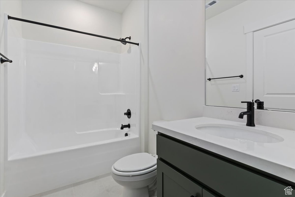 Basement bathroom with tile patterned flooring, vanity, toilet, and shower / washtub combination