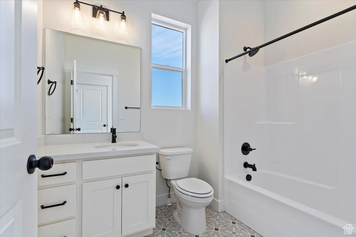 Full main floor bathroom with tile patterned flooring, vanity, toilet, and washtub / shower combination