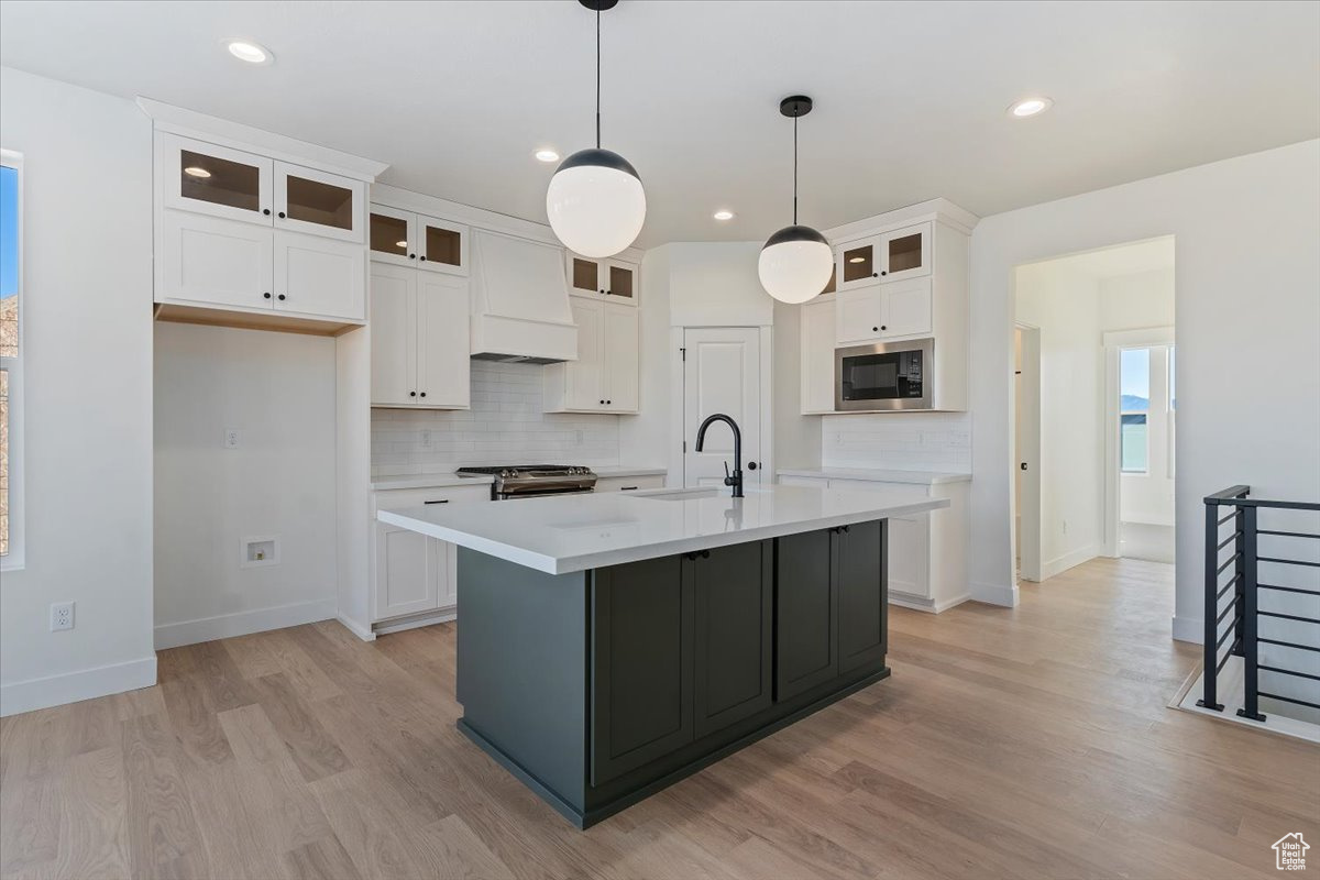 Kitchen with stainless steel gas range, exhaust hood, white cabinets, and designer light fixtures